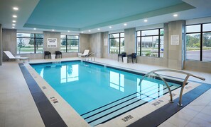 Une piscine intérieure à l’eau claire, avec des zones de profondeur clairement indiquées et des chaises longues.
