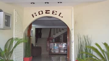 Entrada de hotel con un cartel que dice "ROZEL", una escalera y plantas en macetas.