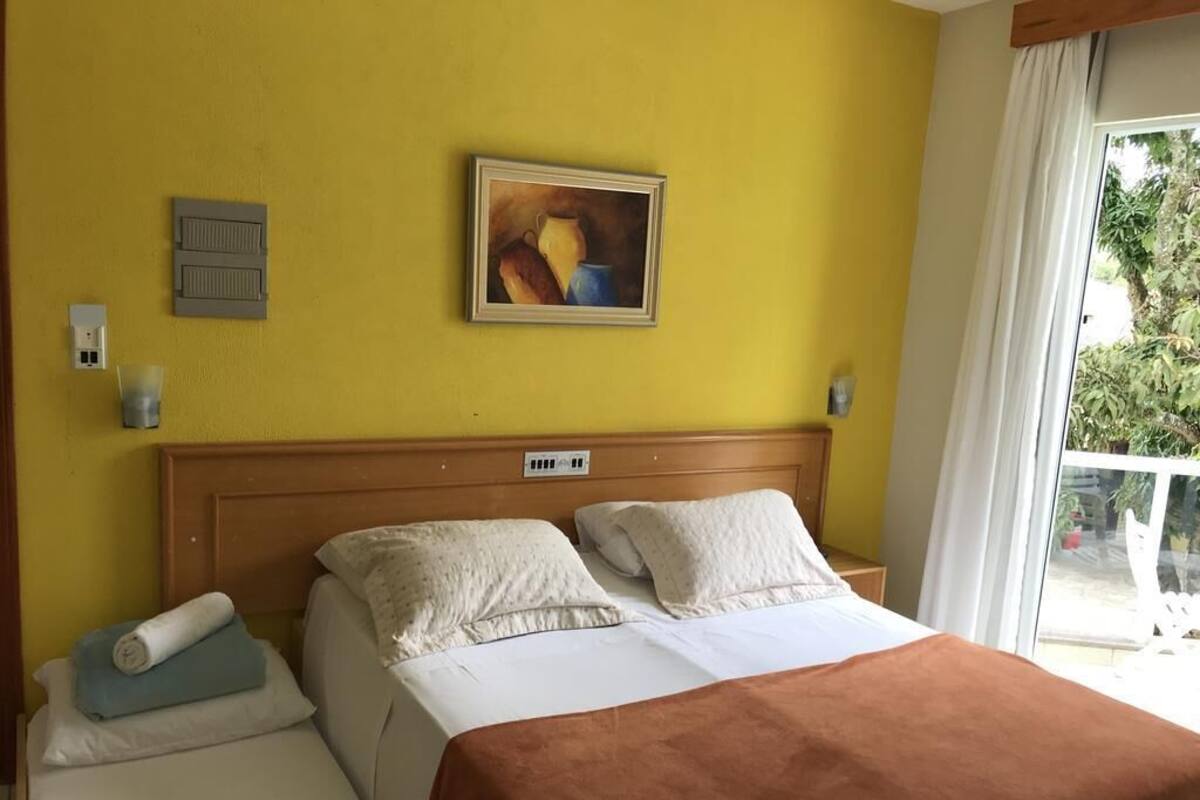 Hotellihuone, jossa on sänky, taulu seinällä ja ikkuna, jossa on verhot.