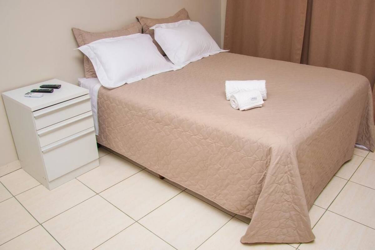 A neatly made bed with a beige quilt, a white pillow, and a folded white towel on the bed.