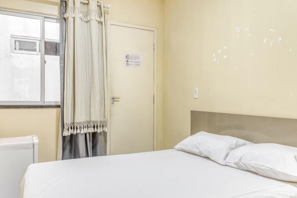 Une chambre à coucher avec un lit, une fenêtre avec des rideaux, une porte avec une pancarte et un thermostat.