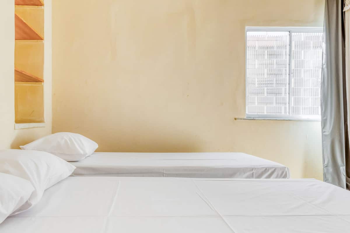 Une chambre avec deux lits, une fenêtre avec des stores et un mur uni.