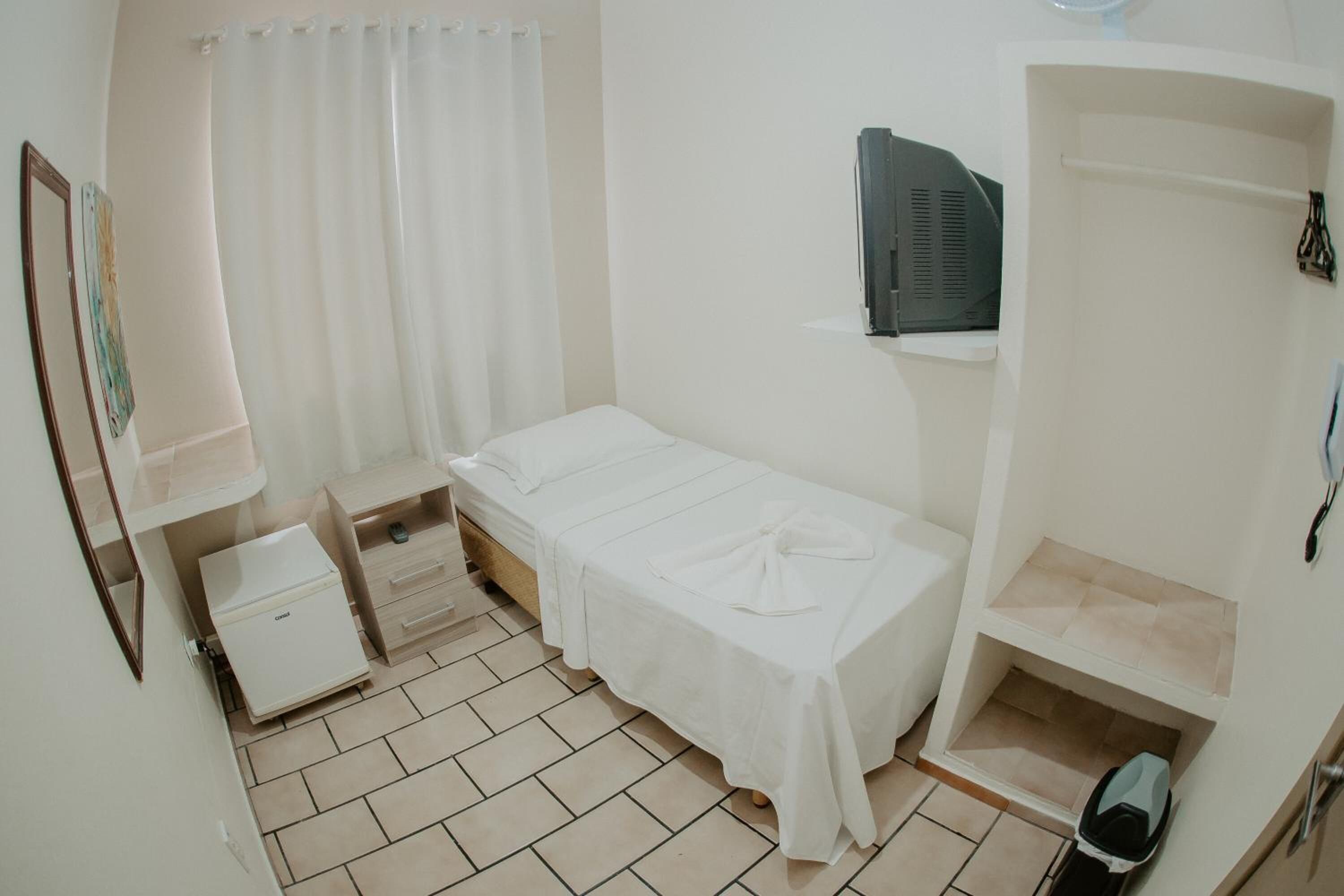 Een kleine, schone kamer met een bed, een bureau, een stoel, een televisie en een kledingkast.