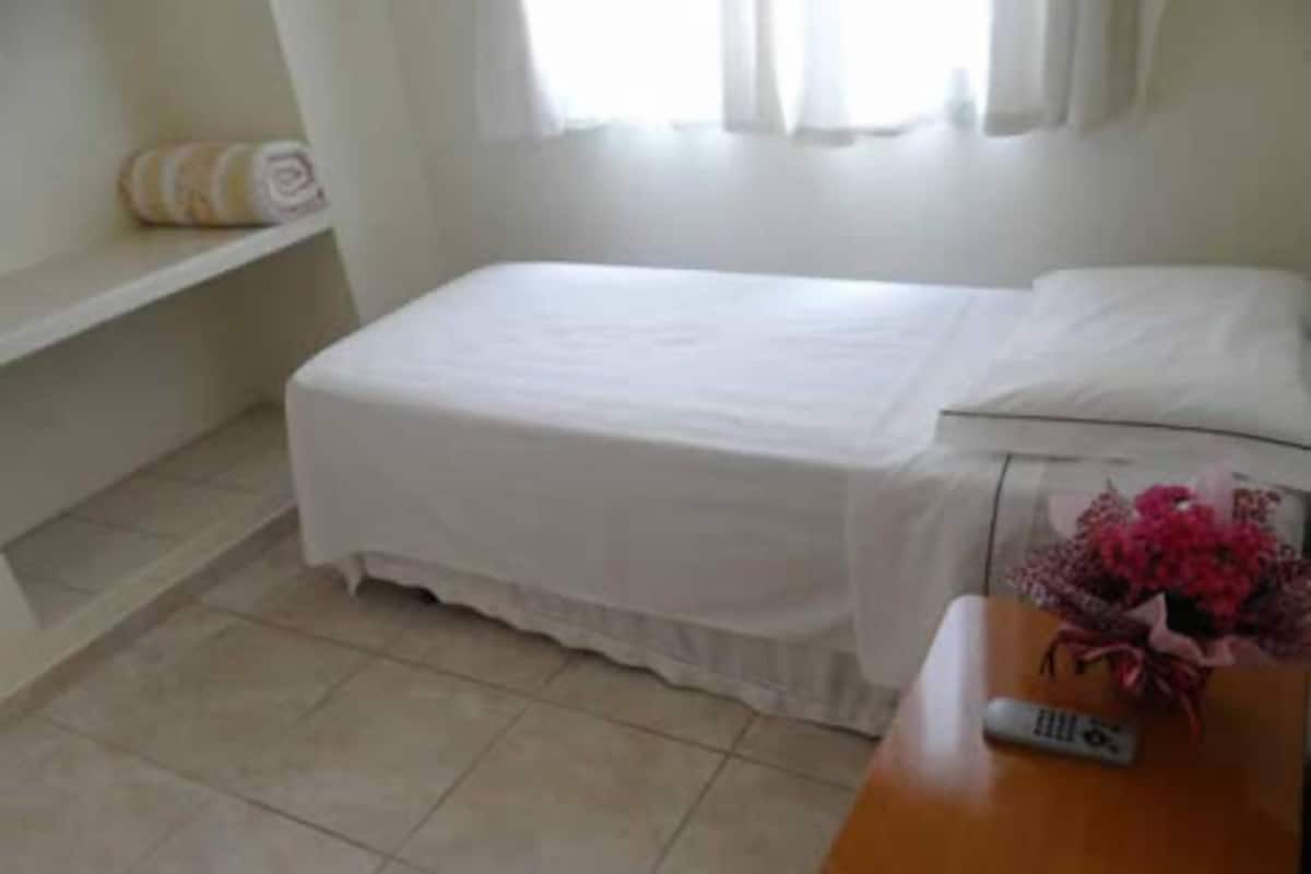 Un dormitorio con cama, mesita de noche y ventana con cortinas.