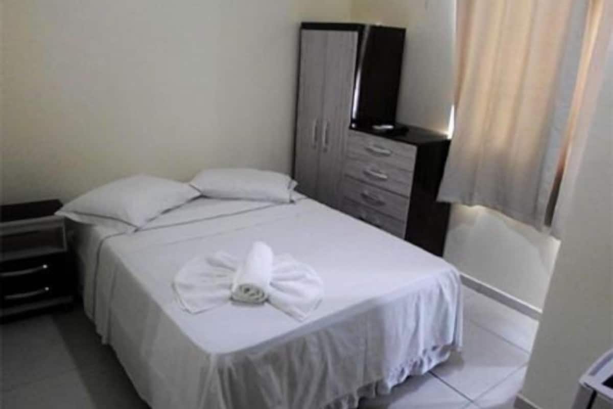 Una habitación de hotel con cama, cómoda, espejo y ventana con cortinas.