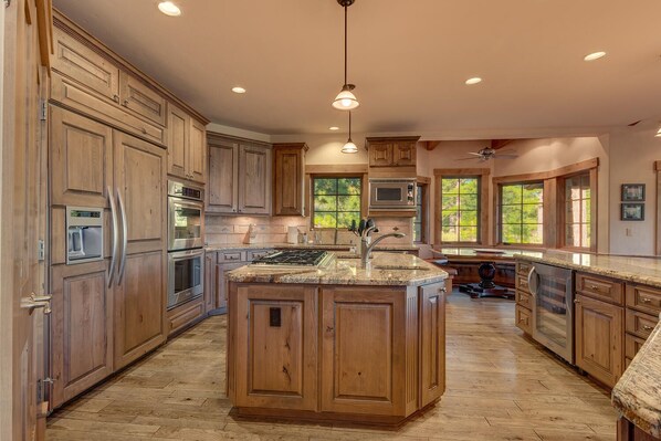 A spacious kitchen with wooden cabinets, stainless steel appliances, a large island, and large windows providing natural light.