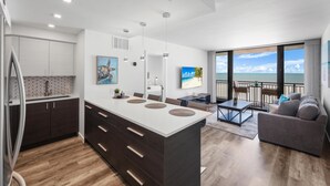 A modern kitchen with a large island, a dining area with a view, and a living room with a sofa. - Modern 11th Floor Beachfront Condo With Views/pool (Marco Island)