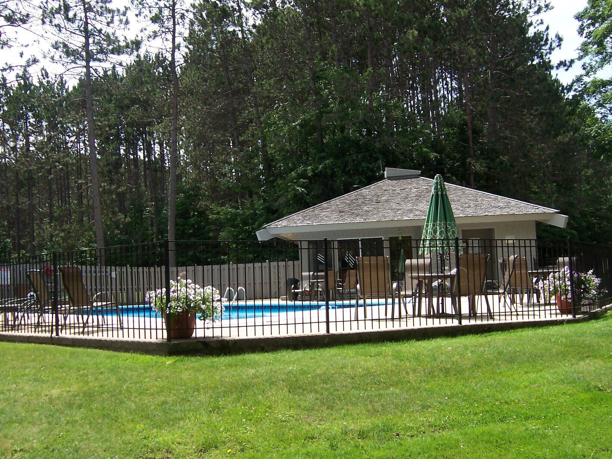 A fenced backyard with a pool, lounge chairs, and a covered patio area.