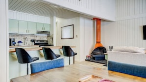 Une cuisine moderne avec des meubles blancs, une table à manger en bois et une grande cheminée orange.