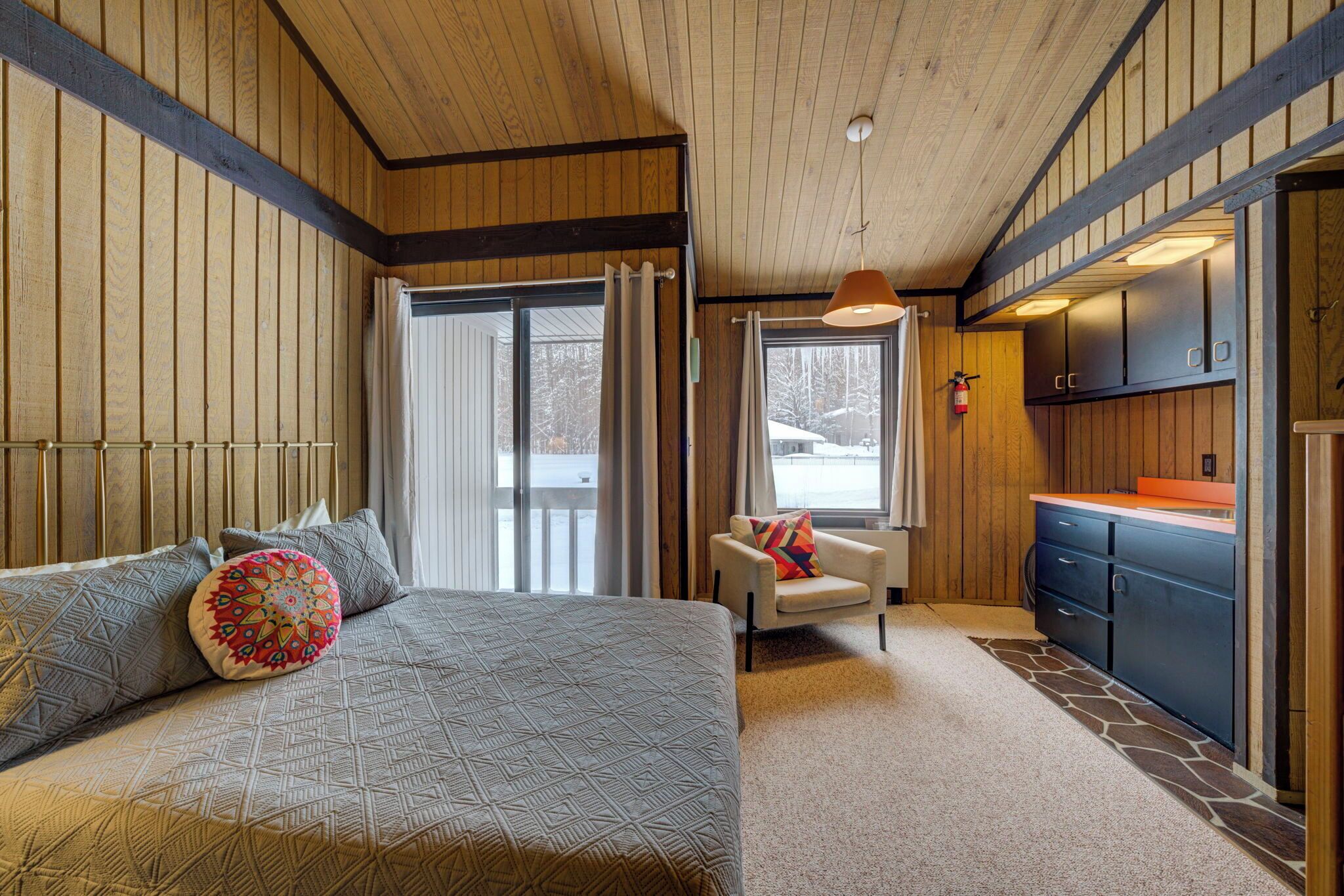 A bedroom with a large bed, a chair, a window, and a kitchen area.
