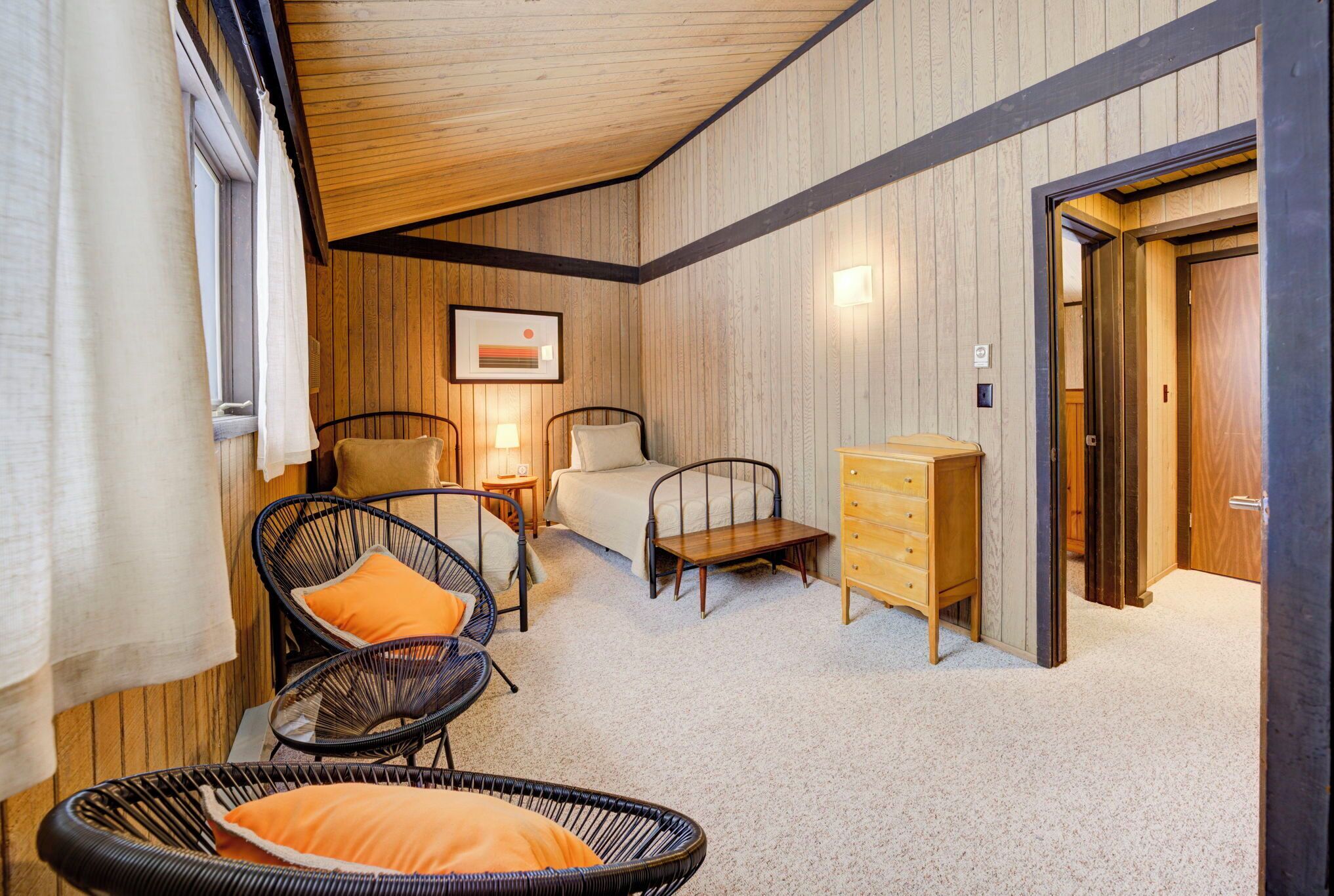 Ein gemütliches Zimmer mit einem Bett, zwei Korbstühlen, einer Holzkommode und einem kleinen Tisch mit einer Lampe.