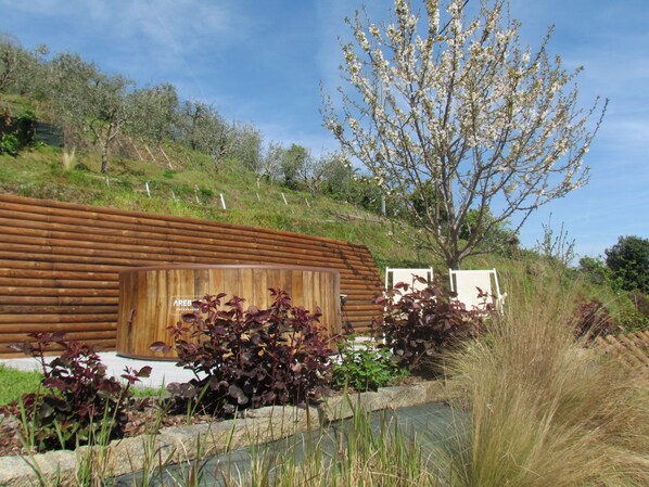 Eine moderne Blockhütte mit Holzfassade, umgeben von einem angelegten Garten mit verschiedenen Sträuchern und einem Baum mit weißen Blüten.