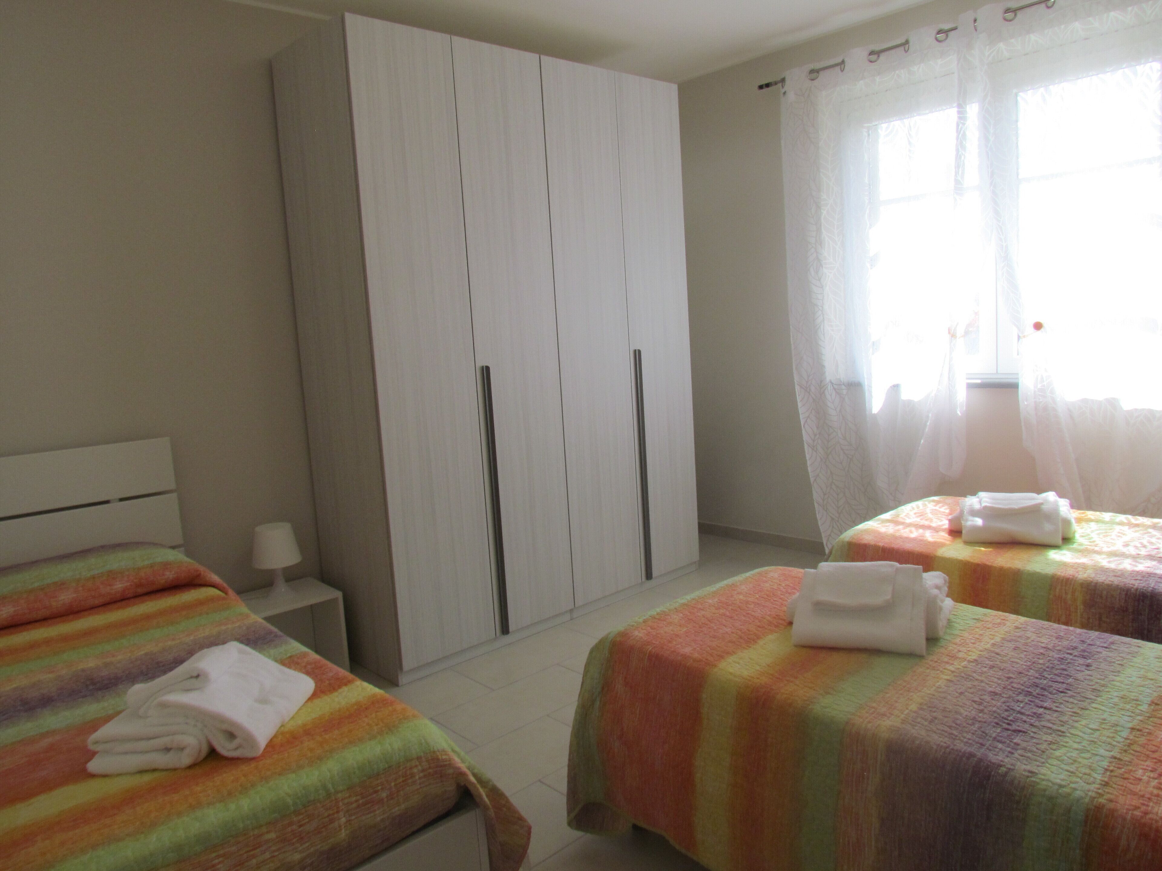 A bedroom with two beds, a wardrobe, and a window with curtains.