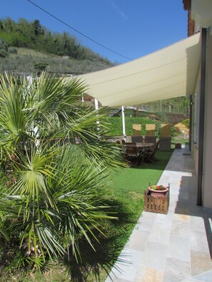 Eine Terrasse mit Tisch, Stühlen, einem Blumentopf und einem Weg zu einem Gebäude.