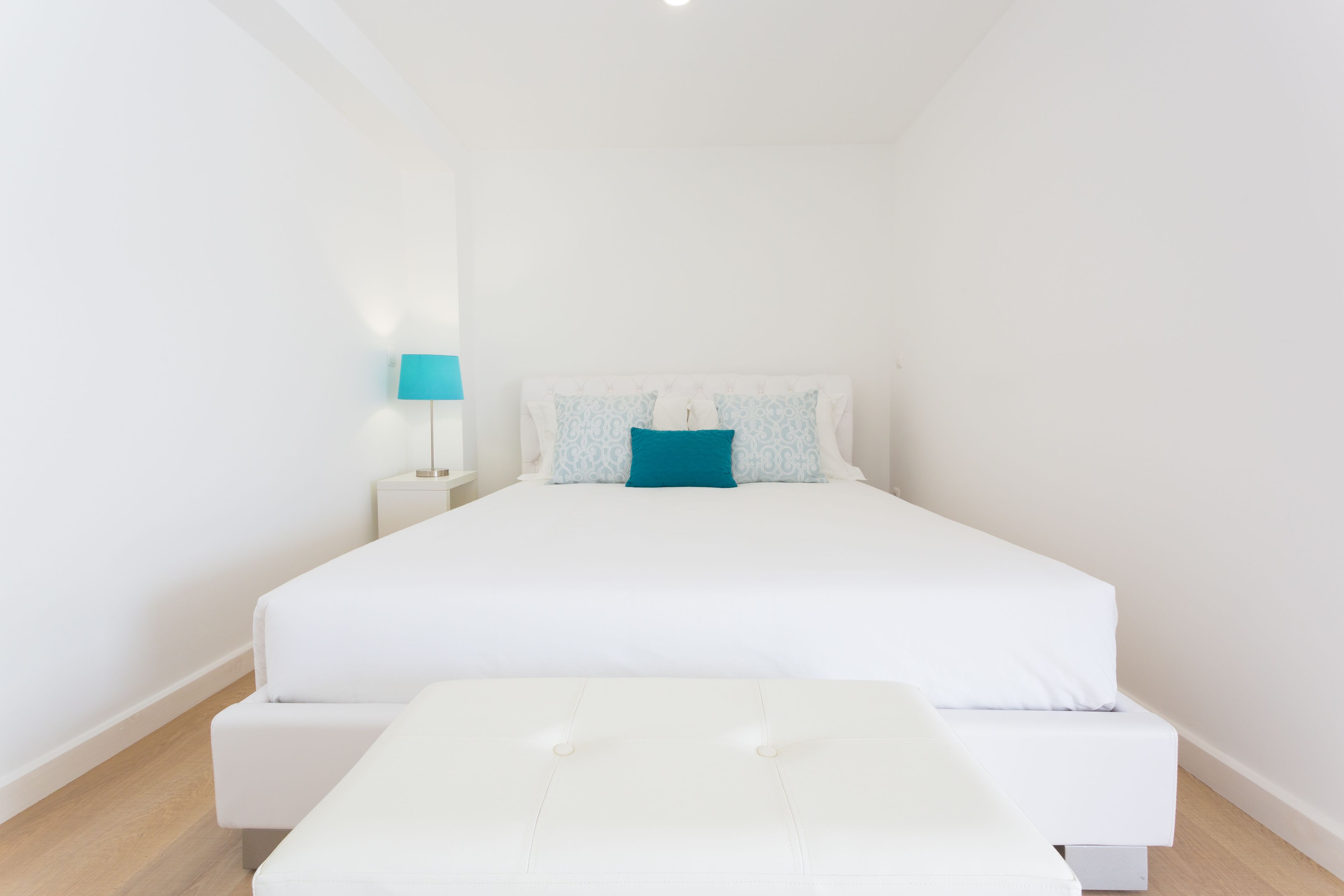 A minimalist bedroom with a large bed, a bedside table with a lamp, and a small bedside table with a lamp.