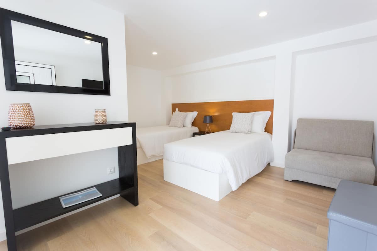 A hotel room with a bed, a sofa, a desk with a mirror, and a bedside table.