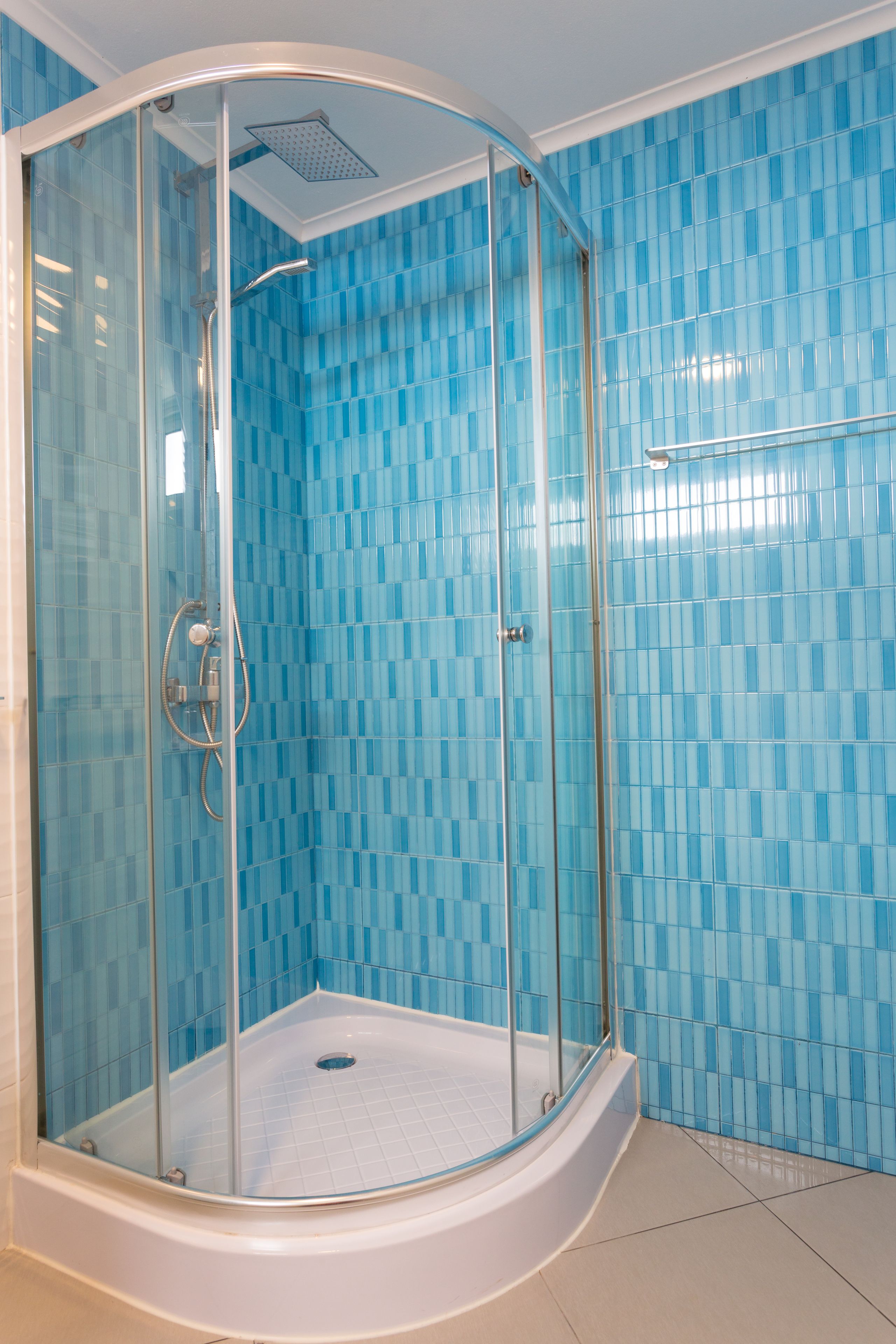 A glass-enclosed shower with a white tub, blue mosaic tiles on the walls, and a white floor.