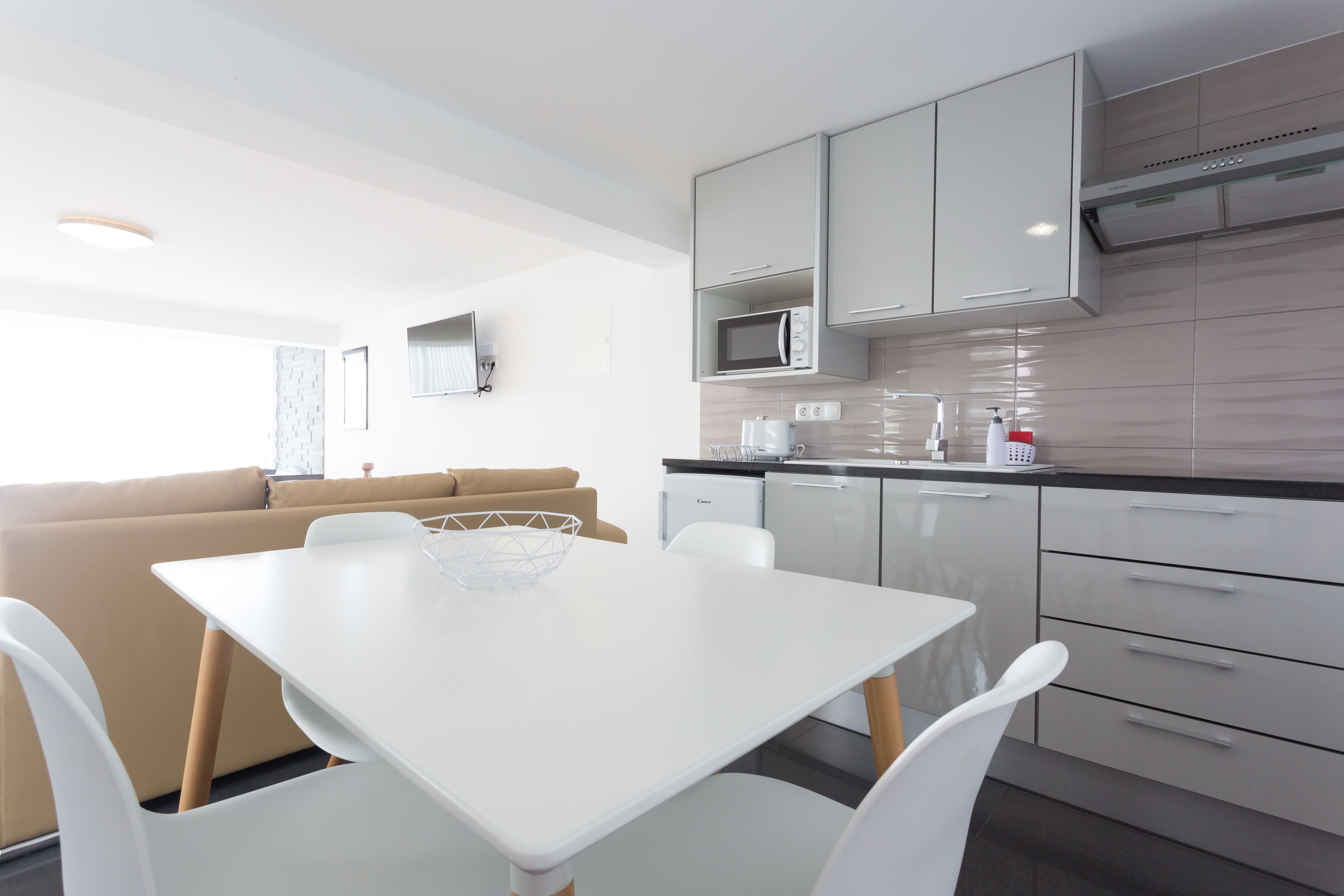 A modern kitchen with white cabinets, a microwave, and a dining area with a white table and chairs.