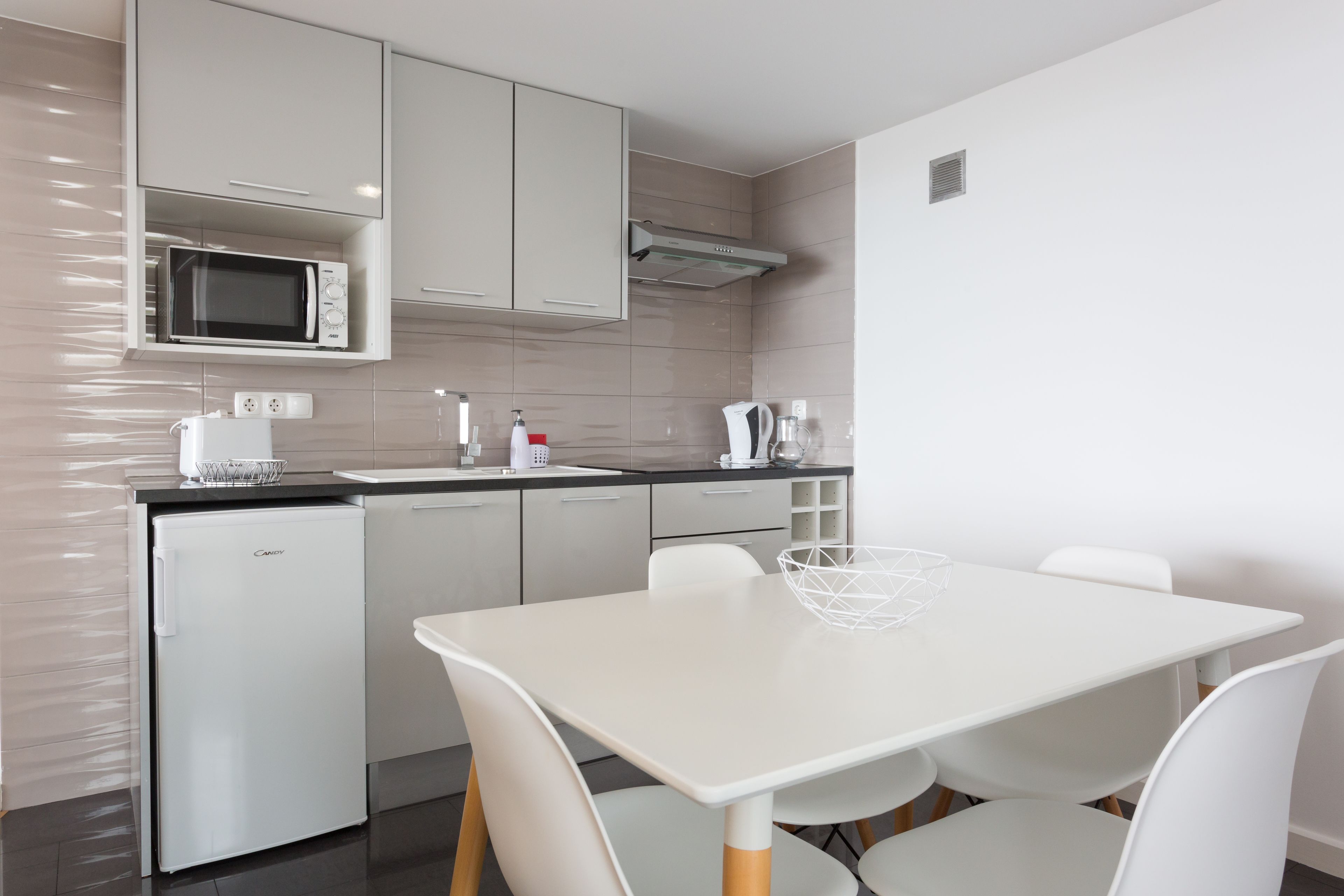Une cuisine moderne avec des meubles blancs, un four à micro-ondes encastré, un réfrigérateur et une table à manger avec des chaises.