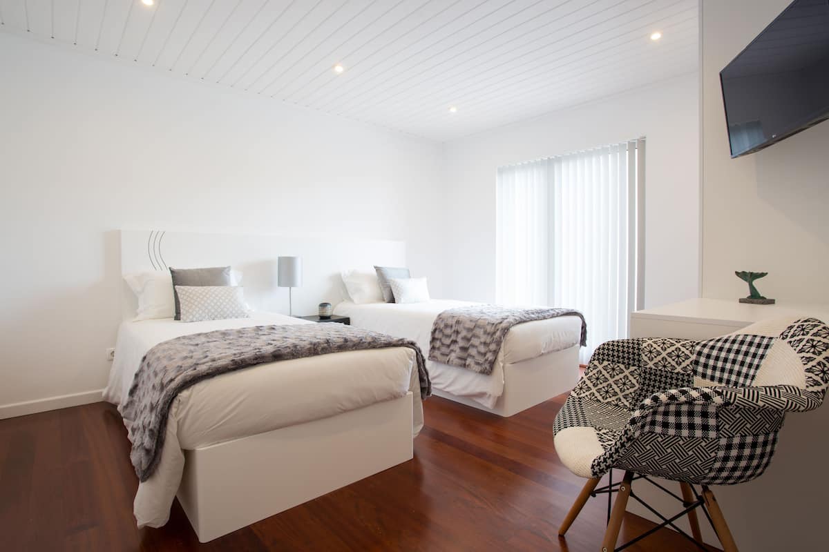 A modern bedroom with two beds, a TV, and a chair.