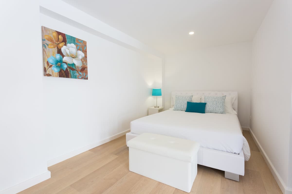 A bedroom with a bed, a nightstand, a lamp, and a painting on the wall.