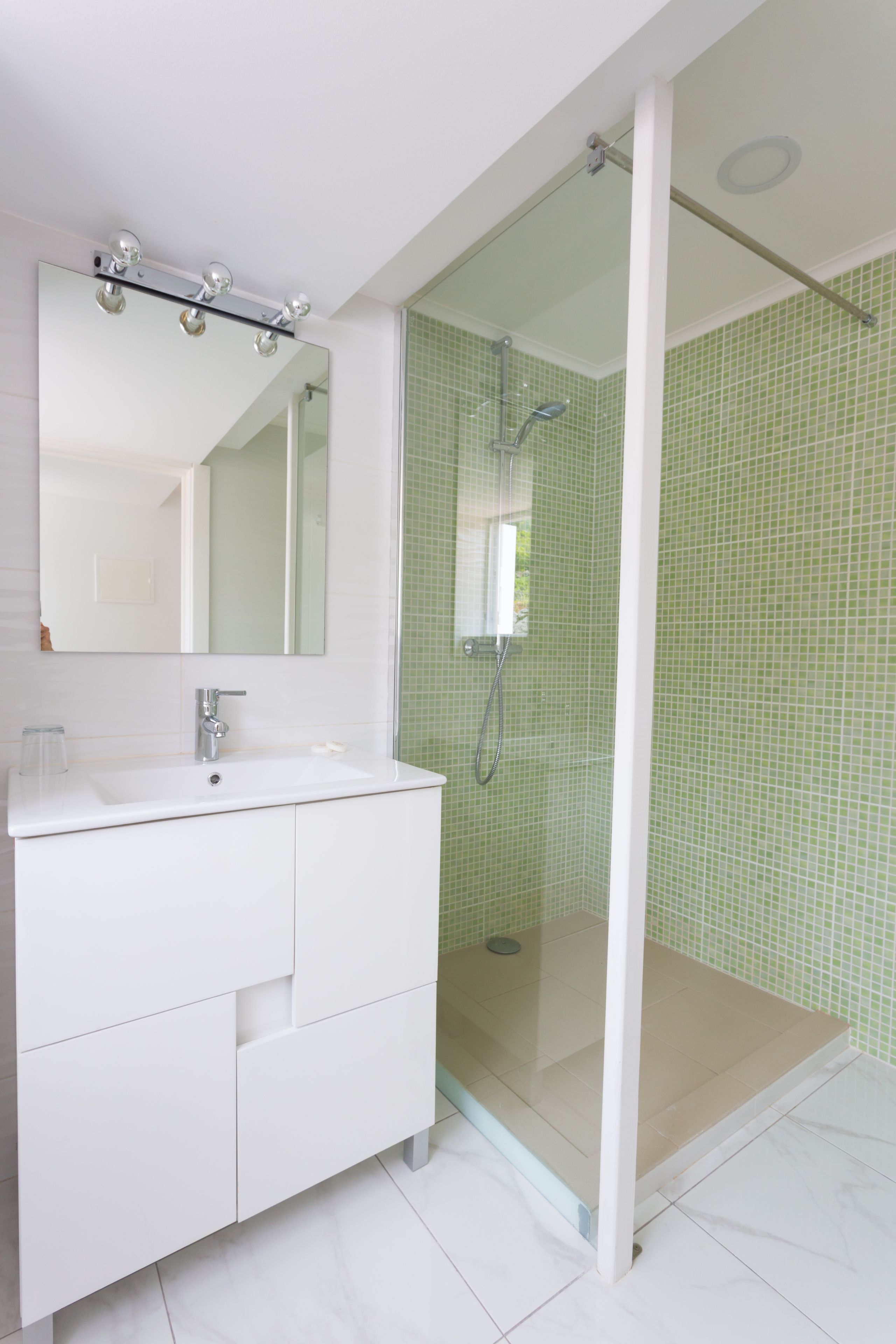 A modern bathroom with a white vanity, a glass-enclosed shower, and green tiled walls.