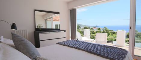 Un dormitorio con cama, cómoda, espejo y balcón con vistas al mar.