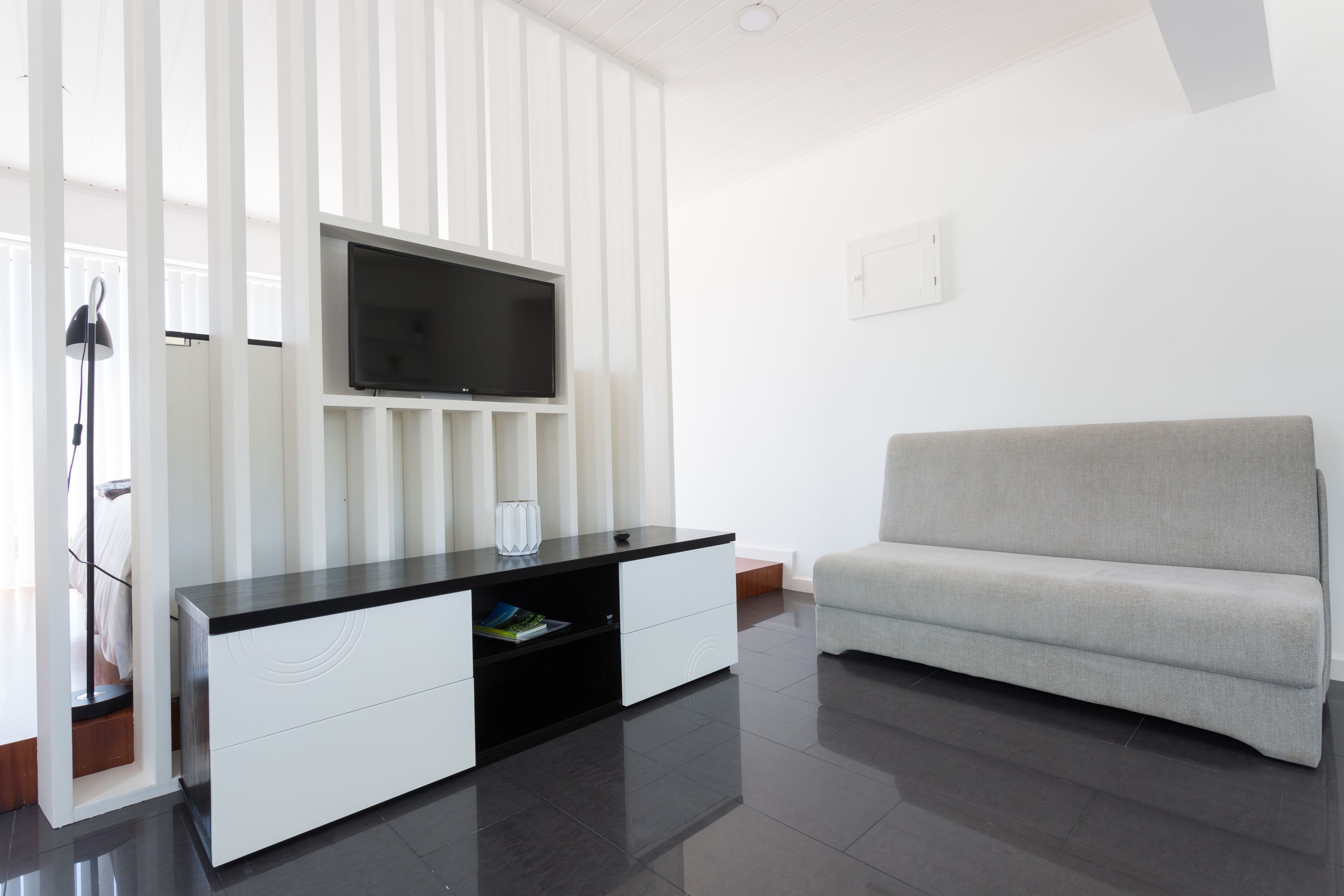 Un soggiorno moderno con una TV a schermo piatto montata su un mobile bianco, un divano grigio e una lampada da terra.