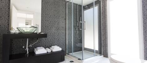 Un baño moderno con ducha de vidrio, un tocador negro con lavabo de vidrio y un inodoro blanco.