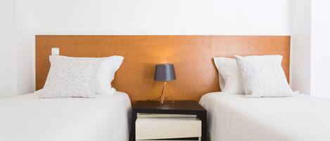 A hotel room with two beds, a nightstand with a lamp, and a wooden headboard.