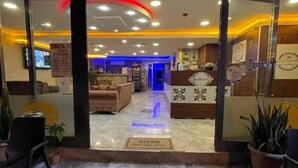 Zona de recepción de hotel con suelo de mármol, mostrador de recepción y área de descanso con sillas y sofá.