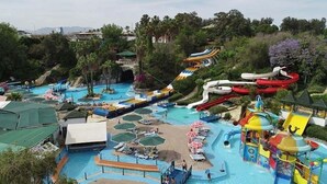 Un parque acuático con varias toboganes y piscinas, rodeado de palmeras y sombrillas.