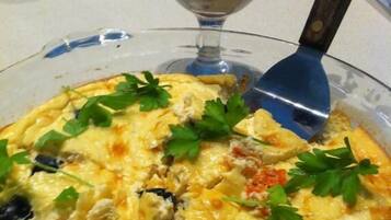 A quiche with parsley garnish, a glass of dessert with berries, and a knife on a table.