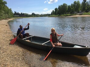 En smal båt med två personer som paddlar på en stilla flod.