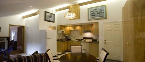 A compact kitchen with wooden cabinets, a dining table with four chairs, and a chandelier.
