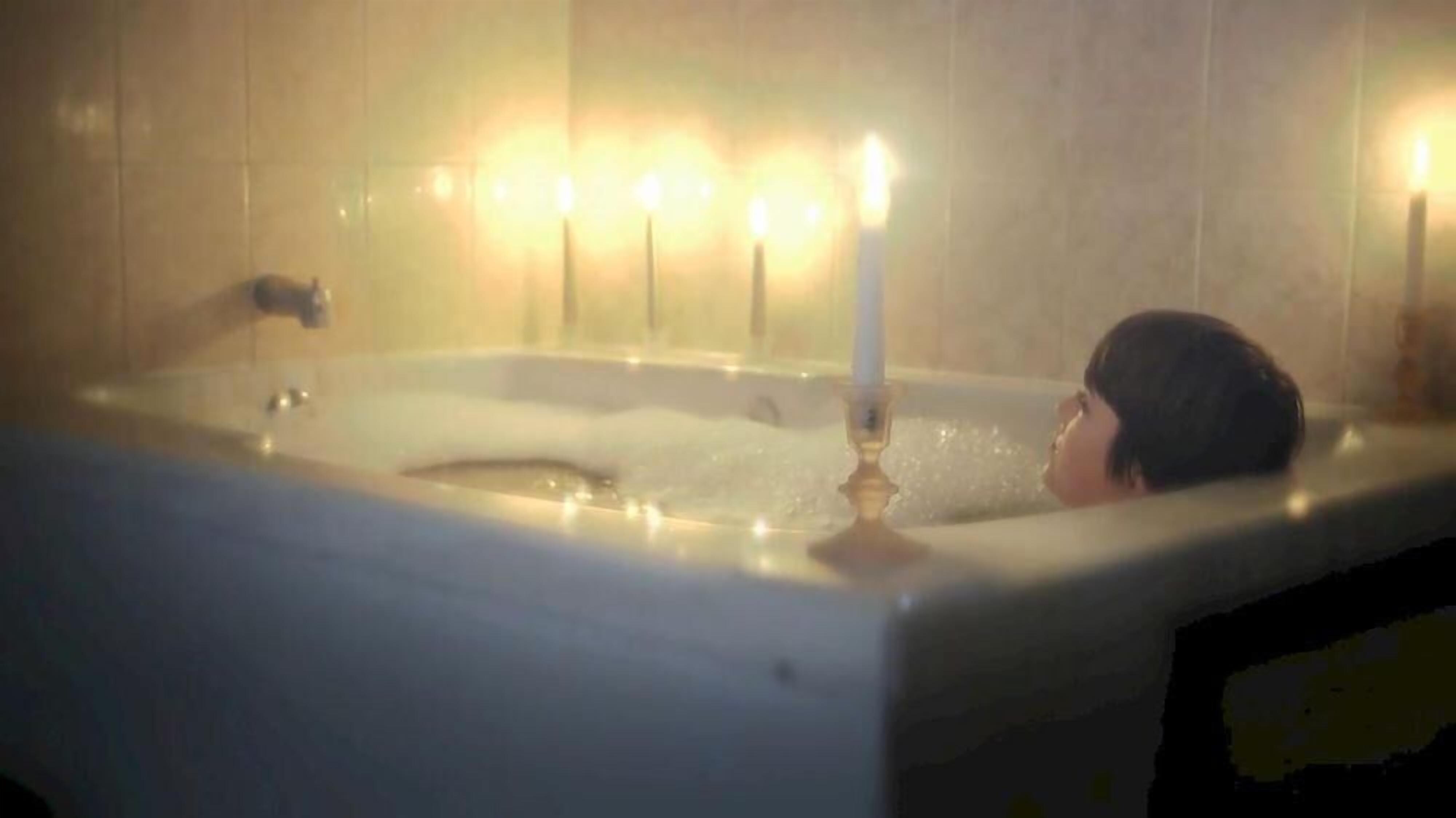 A person in a bathtub with candles.