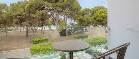 A balcony with a round table and two chairs, overlooking a landscaped area with trees and a distant view of a building.