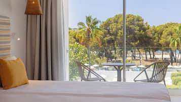 A hotel room with a large bed, a view of a beach, and outdoor seating.