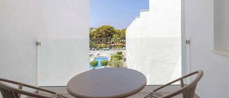 A balcony with a round table and two chairs, overlooking a swimming pool and greenery.