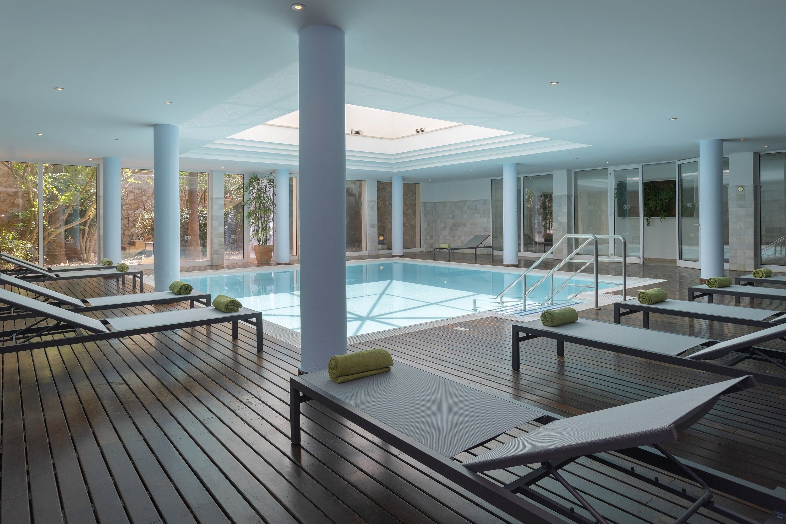 A poolside area with wooden loungers, a glass-enclosed pool, and a view of the outdoors.