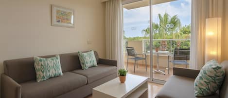 Una sala de estar con un sofá, una mesa de centro y un balcón con vistas a palmeras.