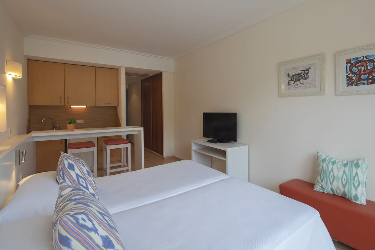 A hotel room with a bed, a TV, a small kitchenette, and a red sofa.
