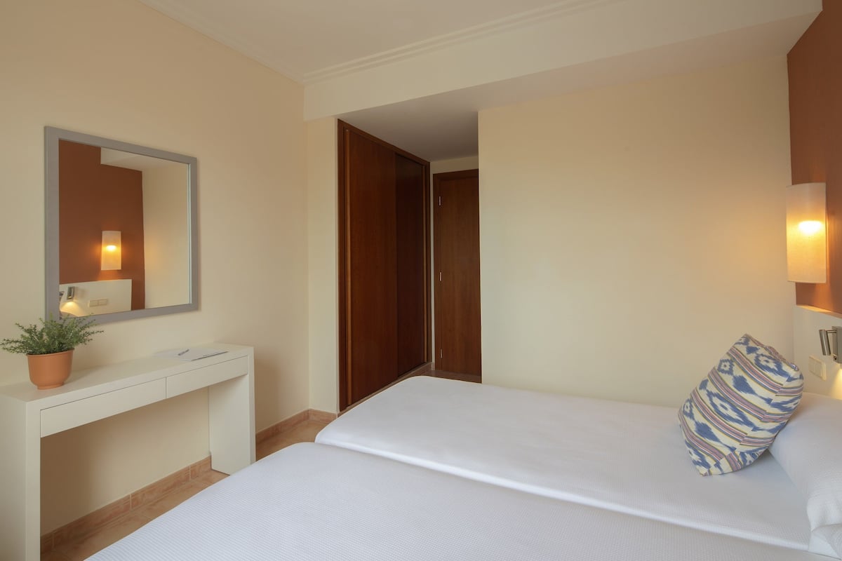 A hotel room with a bed, a bedside table with a plant, a mirror, and a wardrobe.
