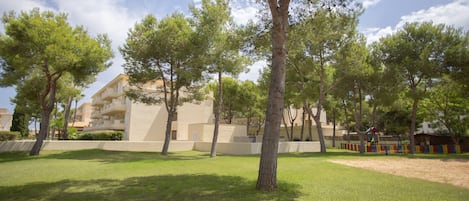 A grassy area with trees and a building with balconies.