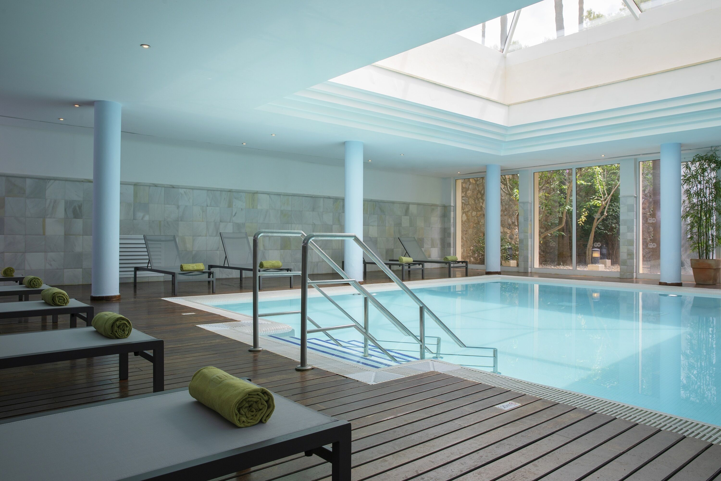 Una piscina interior con cubierta de madera, sillones de descanso y una barandilla de cristal.