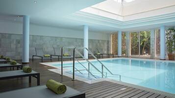 Une piscine intérieure dotée d’une terrasse en bois, de chaises longues et d’une paroi en verre.