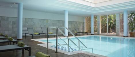 Una piscina interior con cubierta de madera, sillones de descanso y una barandilla de cristal.