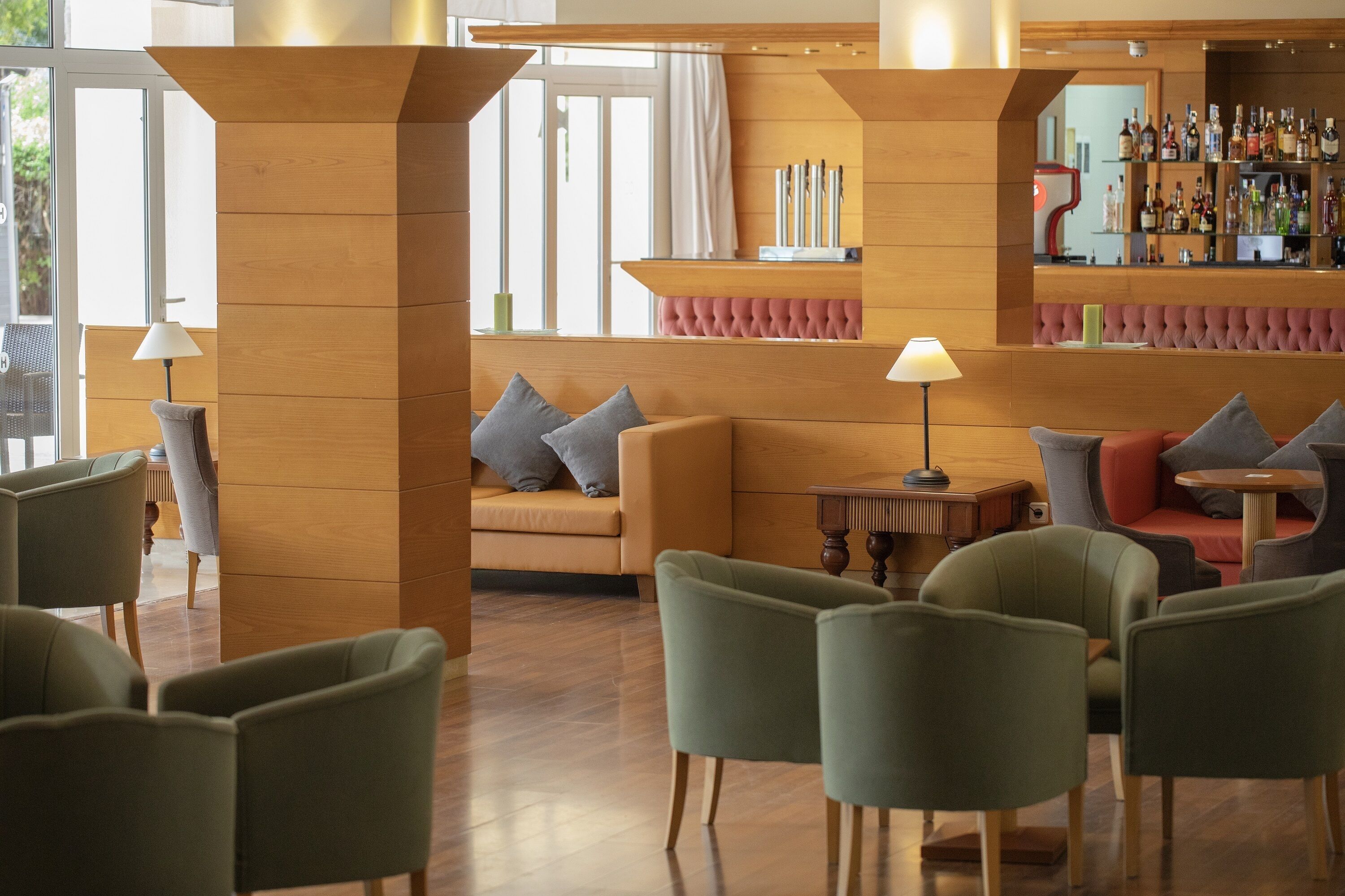 A modern lounge area with wooden columns, a sofa with cushions, and a bar with bottles.