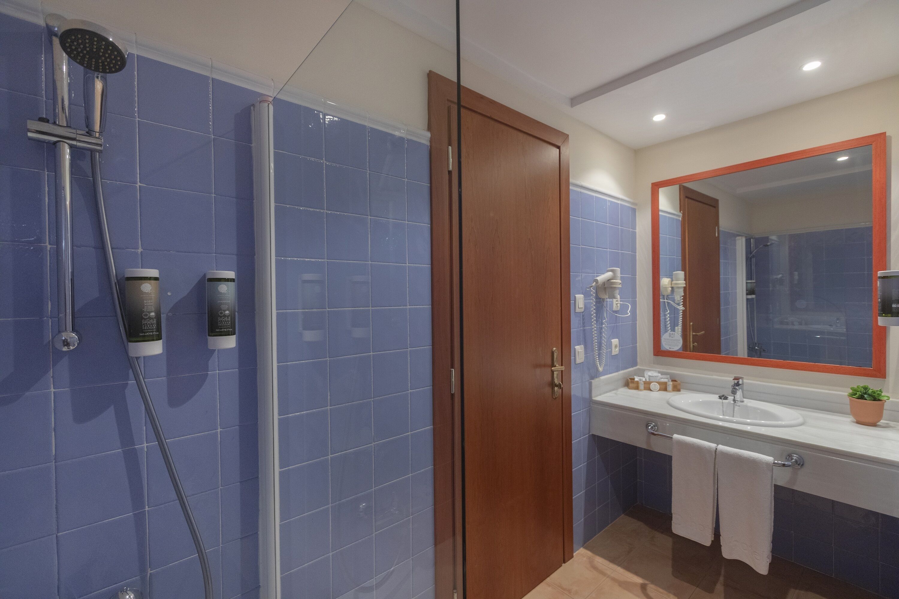 Un baño con ducha, lavamanos y espejo.