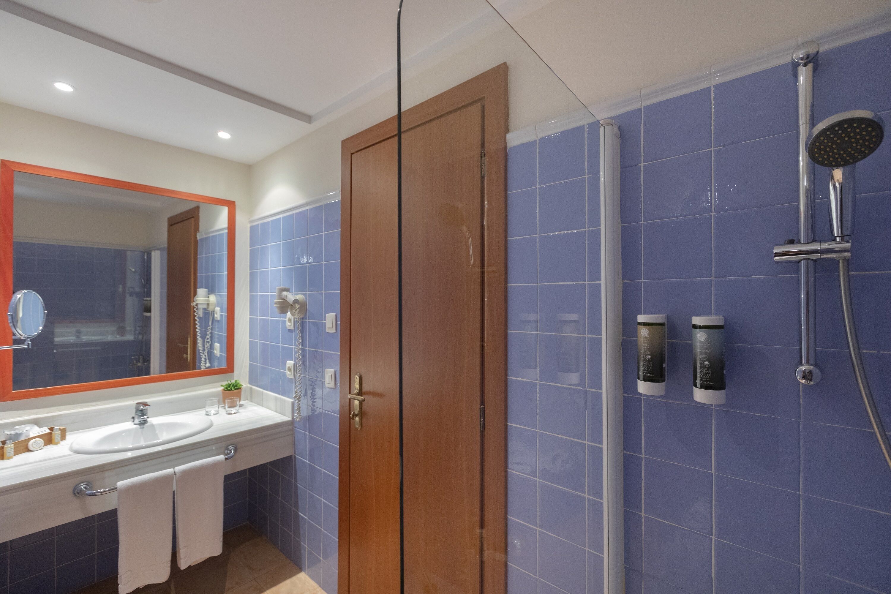 Une salle de bain avec une porte en bois, un lavabo et une douche équipée d’un pommeau de douche amovible.